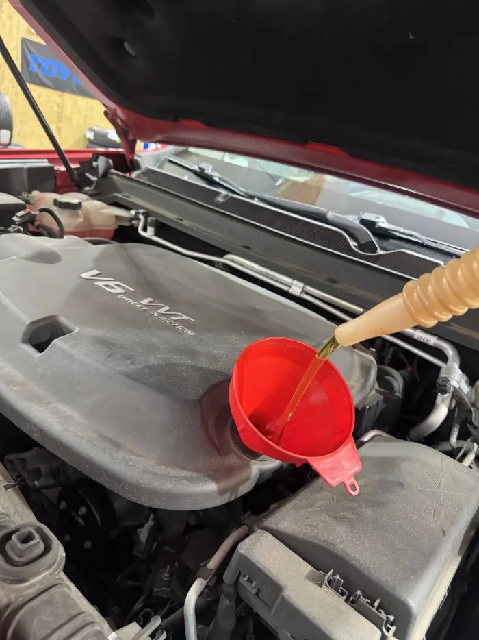 Fresh oil being poured through a funnel into a V6 engine during an oil change